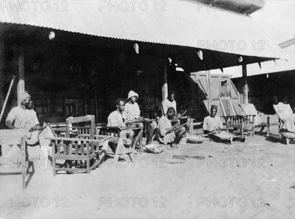 Caning chair frames. Local employees of the Kenyan Public Works Department cane wooden chair frames that were made in their workshop at Nakuru under the supervision of Charles Bungey, a training officer with the PWD. Kenya, 1922. Kenya, Eastern Africa, Africa.