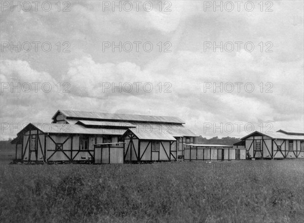 Apprentices' quarters. Several light timber-framed buildings with tin roofs are clustered together in a field, providing housing for apprentices in the Kenyan Public Works Department. They were erected under the supervision of Charles Bungey, a training officer with the PWD. Nakuru, Kenya, 1923. Nakuru, Rift Valley, Kenya, Eastern Africa, Africa.