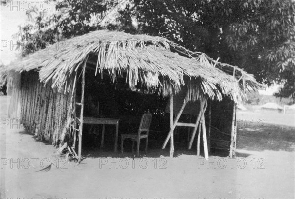 Thatched classroom. A three-walled classroom constructed from wooden poles and a thatched roof. Related images show that this is one of several similar 'rooms' in a compound. Waa, Kenya, 1925. Waa, Coast, Kenya, Eastern Africa, Africa.