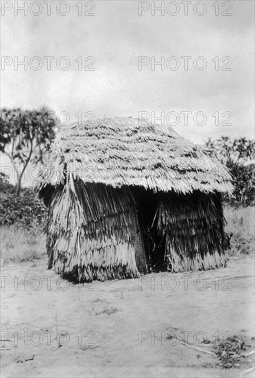 Small thatched classroom. A small thatched classroom constructed from thatch or other grass-like material. A narrow gap in one wall appears to be the doorway. Related images show that is one of several similar 'rooms' in a compound. Waa, Kenya, 1925. Waa, Coast, Kenya, Eastern Africa, Africa.