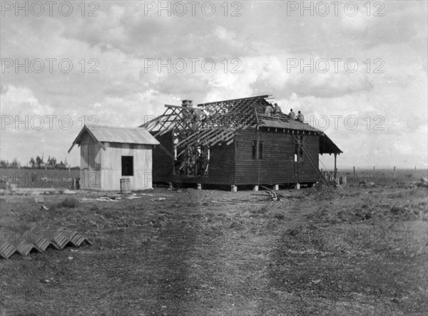 Building a house. This is the second in a series of four photographs showing the rapid erection of a timber-framed European-style house. The photograph is taken from the back, showing the separate kitchen block. The house was built for Charles Bungey, a training officer with the Kenyan Public Works Department, by the local apprentices of his department. Nakuru, Kenya, March 1922. Nakuru, Rift Valley, Kenya, Eastern Africa, Africa.