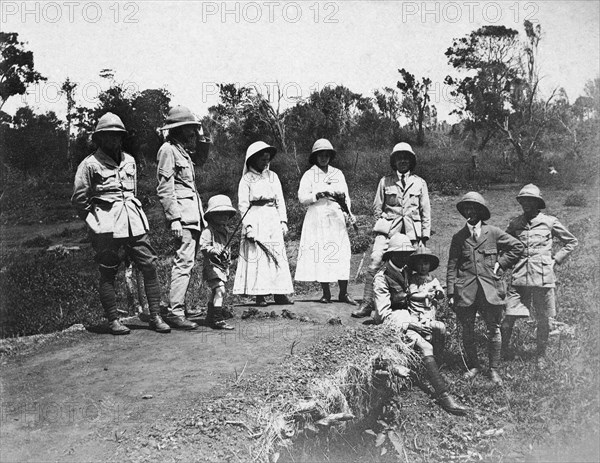 Europeans on an outing. A party of European men, women and children wearing pith hats pose for the camera on a dirt road. Some of the men wear army uniform and the two women wear utilitarian, white dresses. Mbagathi, British East Africa (Kenya), 1916. Mbagathi, Nairobi Area, Kenya, Eastern Africa, Africa.