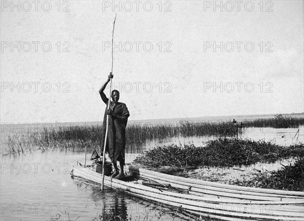 Reed canoe on Lake Victoria. A man stands at the rear of a canoe made from long reeds lashed together, and propels it through the shallows of the lake with a long pole. Lake Victoria, British East Africa (Kenya), circa 1915., Nyanza, Kenya, Eastern Africa, Africa.