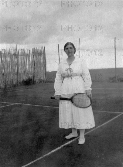 Mrs Bungey on the tennis court. Mrs Bungey, the wife of Charles Bungey, a training officer with the Public Works Department, poses wearing tennis whites with racket in hand on a clay or asphalted tennis court. Nairobi, British East Africa (Kenya), circa 1916. Nairobi, Nairobi Area, Kenya, Eastern Africa, Africa.