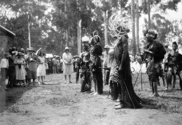 African leaders at the North Kavirondo show. African leaders present themselves to the Governor of Kenya at the North Kavirondo agricultural show. They wear headdresses decorated with split hippopotamus tusks, animal hides and hold ostrich eggs. European onlookers are in the background. Mumias, Kenya, January 1931. Mumias, West (Kenya), Kenya, Eastern Africa, Africa.