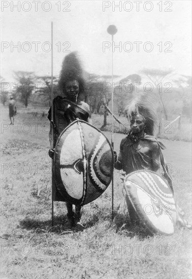 Nandi film extras. Two Nandi warriors recruited as film extras for the 1930 film 'Africa Speaks'. They wear elaborate traditional costumes and pose with shields, spears and staffs. Kapsabet, Kenya, 1928. Kapsabet, Rift Valley, Kenya, Eastern Africa, Africa.