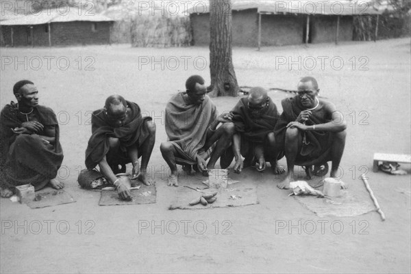 Snuff sellers at Machakos. Five snuff sellers squat on the road, their wares spread out on small cloths in front of them. Machakos, Kenya, 1927. Machakos, East (Kenya), Kenya, Eastern Africa, Africa.
