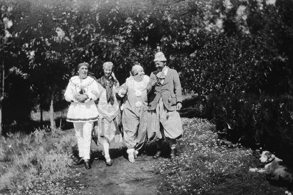 Christmas fancy dress. Four Europeans stroll arm-in-arm down a garden path wearing fancy dress. Charles Bungey (far left) and his wife (third left) wear clown's costumes. Machakos, Kenya, December 1926. Machakos, East (Kenya), Kenya, Eastern Africa, Africa.