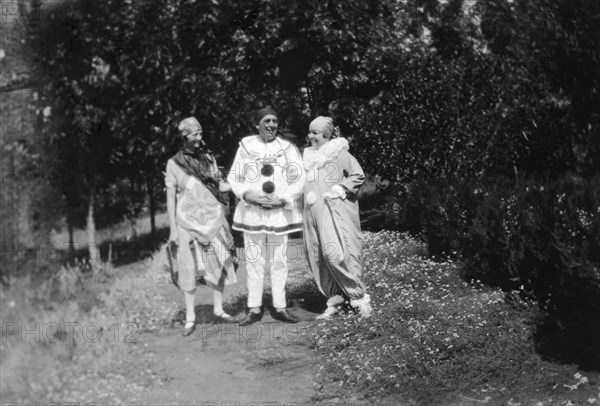Christmas fancy dress. Three Europeans pose on a garden path wearing fancy dress. Charles Bungey (centre) and his wife (right) wear clown's costumes. Machakos, Kenya, December 1926. Machakos, East (Kenya), Kenya, Eastern Africa, Africa.
