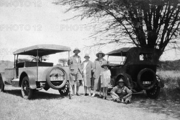 Roadside halt. Informal group portrait of a European family and friends on the roadside between two open-sided cars. A caption records that they are on their way to Sir R. Shaw's estate of 'Bondoni' in Machakos district. Machakos, Kenya, 1927. Machakos, East (Kenya), Kenya, Eastern Africa, Africa.
