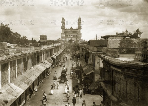 View of the Charminar. A busy street leads up to the Charminar monument, flanked on either side by buildings with shutters and awnings. An important landmark in Hyderabad, the monument lies at the centre of a thriving market, attracting people and merchandise of every description. Hyderabad, India, circa 1905. Hyderabad, Andhra Pradesh, India, Southern Asia, Asia.