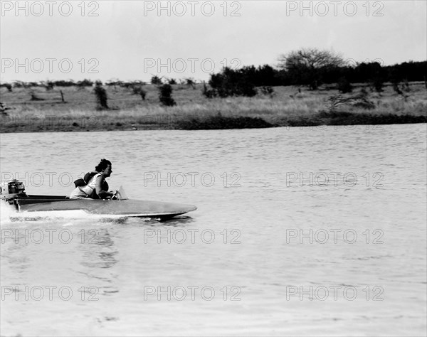 Mrs Archer pilots a speedboat. Mrs Archer scuds across a lake in a small speedboat during a race at the aquasports club meeting. Nairobi, Kenya, 10 September 1955. Nairobi, Nairobi Area, Kenya, Eastern Africa, Africa.
