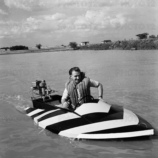 Danny Seales in a striped speedboat. Danny Seales motors across a lake in a small striped speedboat at the aquasports club meeting. Nairobi, Kenya, 14 August 1955. Nairobi, Nairobi Area, Kenya, Eastern Africa, Africa.