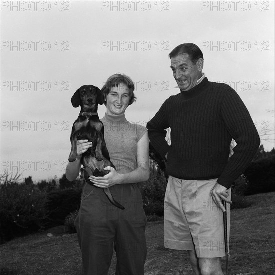 The Thornley Dyer Family. Mr Thornley Dyer leans on a golf club beside his daughter as she poses for the camera holding a pet dachshund dog. Kenya, 4 September 1955. Kenya, Eastern Africa, Africa.