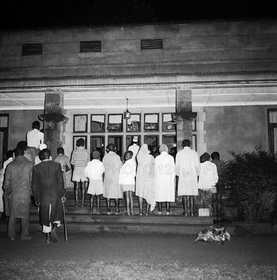 Exclusive entry at the SJAK dance. A group of African spectators watch a dance held for the Sports Journalists Association of Kenya (SJAK) through a window on the outside a building. Kenya, 19 August 1955. Kenya, Eastern Africa, Africa.