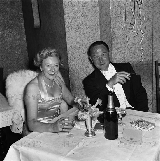 Couple at the SJAK dance. A couple dressed in formal evening wear enjoy a glass of wine at a dance held for the Sports Journalists Association of Kenya (SJAK). A pamphlet on the table reads: Westwood Park Hotel. Kenya, 19 August 1955. Kenya, Eastern Africa, Africa.