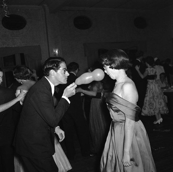 Balloon antics. A straight-faced man brandishes a party balloon in the face of his surprised dance partner at a dance held for the Sports Journalists Association of Kenya (SJAK). Kenya, 19 August 1955. Kenya, Eastern Africa, Africa.
