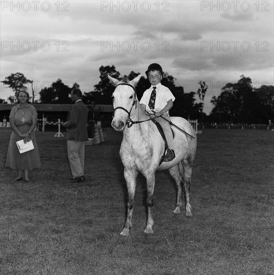 Pony competition at the SJAK show. A young boy sits astride a pony in the class two child's pony competition at the SJAK show (Sports Journalists Association of Kenya). Kenya, 20 August 1955. Kenya, Eastern Africa, Africa.