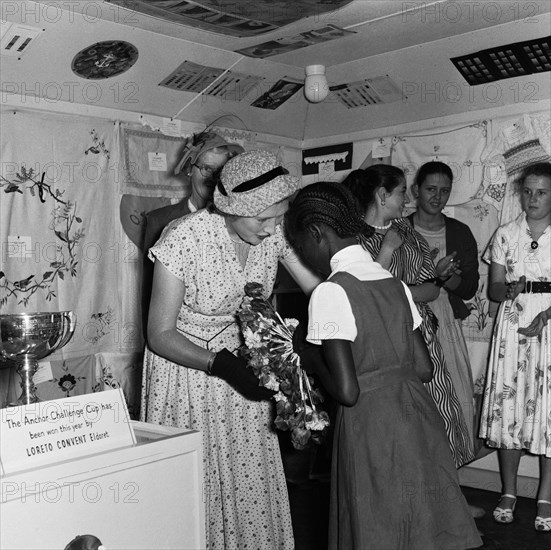 Coats and Clark prizegiving. A young African schoolgirl receives a flower arrangement as a prize from a European woman on the Coats and Clark stand at the Royal Show. Nairobi, Kenya, 28 September-1 October 1955. Nairobi, Nairobi Area, Kenya, Eastern Africa, Africa.