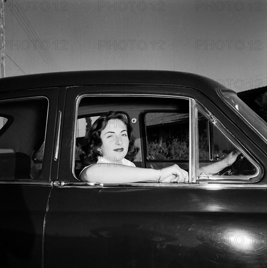 Sue Paton in her MG. Sue Paton smiles from the driver's seat of her MG car, her elbow resting on the open window. Kenya, 24 October 1955. Kenya, Eastern Africa, Africa.