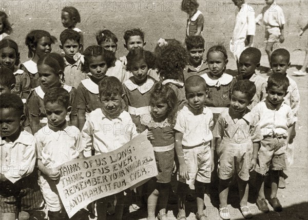 Sudanese schoolchildren. Two boys at the front of a group of African schoolchildren in uniform hold up a sign written in English that reads: THINK OF US LONG: THINK OF US EVER: REMEMBER YOUR NAHDA SCHOOL, AND MARK IT FOREVER. El Obeid, Sudan, 1942. El Obeid, North Kurdufan, Sudan, Eastern Africa, Africa.