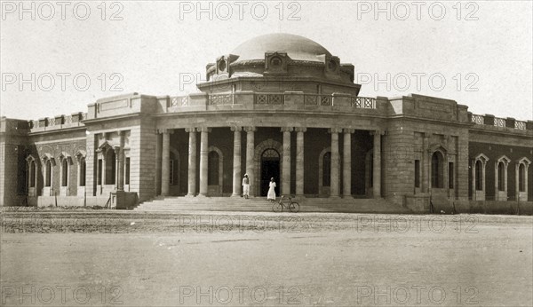 Medical school, Khartoum. Two men stand on the steps of the Khartoum medical school alongside a stretch of open ground. The building displays a central dome, balustrades and pillars. Khartoum, Sudan, circa 1925. Khartoum, Khartoum, Sudan, Eastern Africa, Africa.