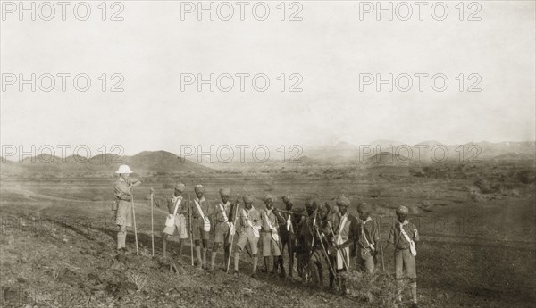 African scout group. A group of African scouts pause during a hike into the country with their European scout leader. Each carries a stick and knapsack and wears a uniform consisting of short trousers, a shirt with neckscarf and long socks. Sinkat, Sudan, 1926. Sinkat, Red Sea, Sudan, Eastern Africa, Africa.