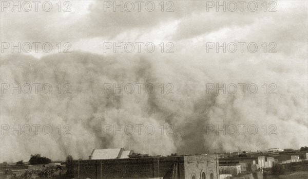 Sudanese sandstorm. A giant cloud of sand engulfs a townscape during a sandstorm. Sudan, circa 1925. Sudan, Eastern Africa, Africa.