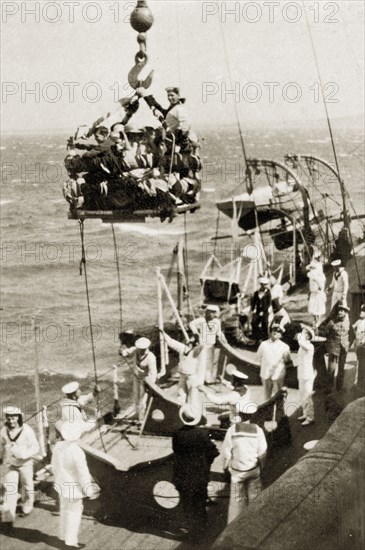 Children's party on the high seas. A group of children packed tightly onto a small platform are hoisted into the air by naval personnel at a children's party aboard HMS Repulse. The date suggests the celebration was for Christmas or New Year. Atlantic Ocean near Cape Town, South Africa, 22-29 December 1923., West Cape, South Africa, Southern Africa, Africa.