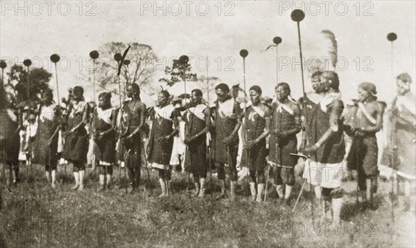 African dancers in costume. A group of African men dressed in ceremonial costume hold sticks as they prepare to perform a traditional dance. Nairobi, Kenya, 12-17 January 1924. Nairobi, Nairobi Area, Kenya, Eastern Africa, Africa.