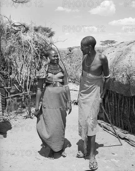 Lepuipui with a Samburu woman. A Samburu man identified as 'Lepuipui' chats to a young Samburu woman in a village. Both wear traditional dress: her's decorated with striking, ornate jewellery. Wamba, Kenya, 13 October 1956. Wamba, Rift Valley, Kenya, Eastern Africa, Africa.