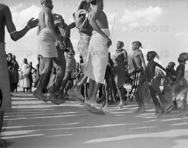 Turkana dancers mid-jump. Turkana adults and children wearing traditional dress are captured mid-jump as they perform a 'ngoma'. Wamba, Kenya, 13 October 1956. Wamba, Rift Valley, Kenya, Eastern Africa, Africa.