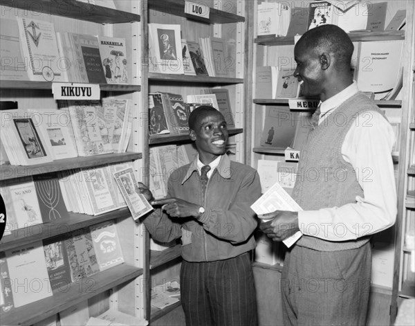 Kenyan book shop. Promotional shot for the East African Literature Bureau. Two African men exchange smiles in a bookshop as one of them tries to sell a book to the other. Kenya, 25 September 1956. Kenya, Eastern Africa, Africa.