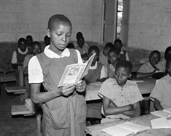 Reading out loud. Promotional shot for the East African Literature Bureau. An African schoolgirl reads out loud to her classmates from a new book produced by the East African Literature Bureau. Kenya, 25 September 1956. Kenya, Eastern Africa, Africa.