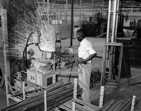 Ideal Casements worker. An African factory worker send sparks flying as he manoeuvres a metal frame into a machine at tool manufacturers Ideal Casements (E.A.) Ltd. Kenya, 11 Oct 1956. Kenya, Eastern Africa, Africa.