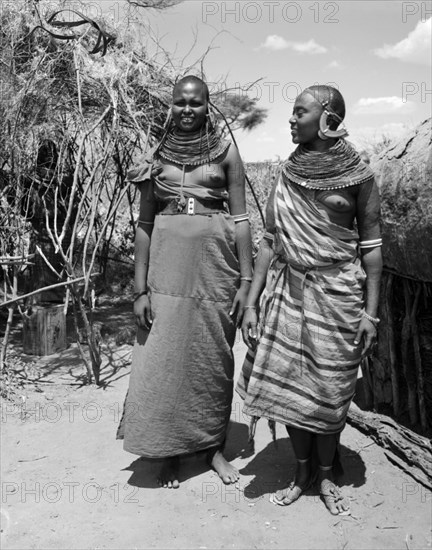 Two Samburu women. Portrait of two young Samburu women in a village. Both wear traditional dress, the most prominent feature of which is their jewellery which consists of heavily beaded necklaces and striking, ornate earrings. Wamba, Kenya, 13 October 1956. Wamba, Rift Valley, Kenya, Eastern Africa, Africa.