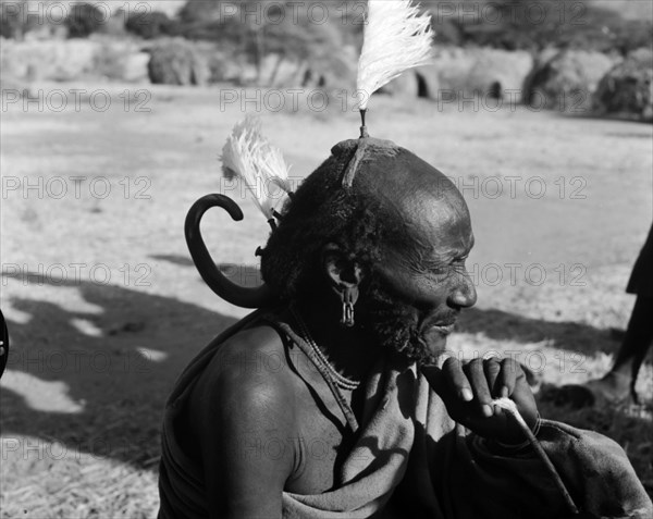 An elderly Turkana man. Portrait of an elderly Turkana warrior, his hair braided and decorated with feathers. He wears an unusual curved hair ornament at the back of his head. Wamba, Kenya, 13 October 1956. Wamba, Rift Valley, Kenya, Eastern Africa, Africa.
