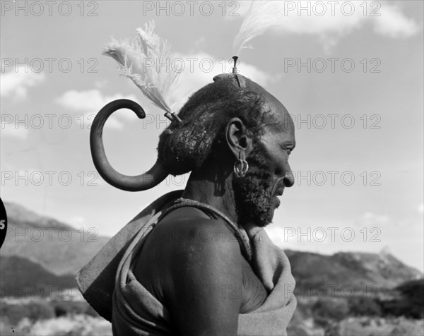 A Turkana headdress. Profile portrait of an elderly Turkana warrior, his hair braided and decorated with feathers. He wears an unusual curved hair ornament at the back of his head. Wamba, Kenya, 13 October 1956. Wamba, Rift Valley, Kenya, Eastern Africa, Africa.