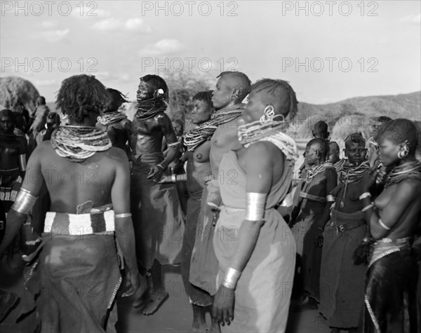 A Turkana 'ngoma'. A group of Turkana adults dance at a crowded 'ngoma'. They wear traditional dress and ornate jewellery including metal armrings, heavily beaded necklaces and earrings. Wamba, Kenya, 13 October 1956. Wamba, Rift Valley, Kenya, Eastern Africa, Africa.