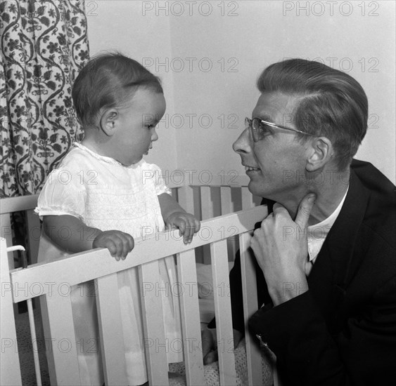 Peter Murdock and his baby. Peter Murdock's baby holds onto the side of a cot, gazing into the eyes of his father. Kenya, 15 October 1956. Kenya, Eastern Africa, Africa.