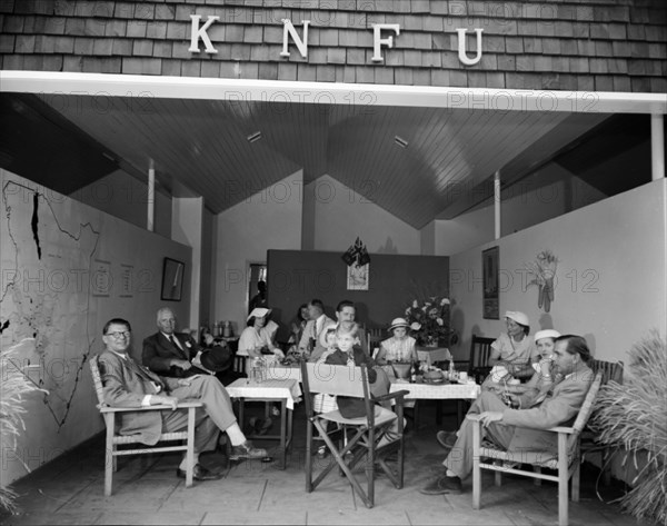 The KNFU at the Royal Show. A group of Europeans sit around tables at the KNFU (Kenya National Famers Union) display stand at the Royal Show. A map of Kenya is displayed on the wall. Kenya, 17-20 October 1956. Kenya, Eastern Africa, Africa.