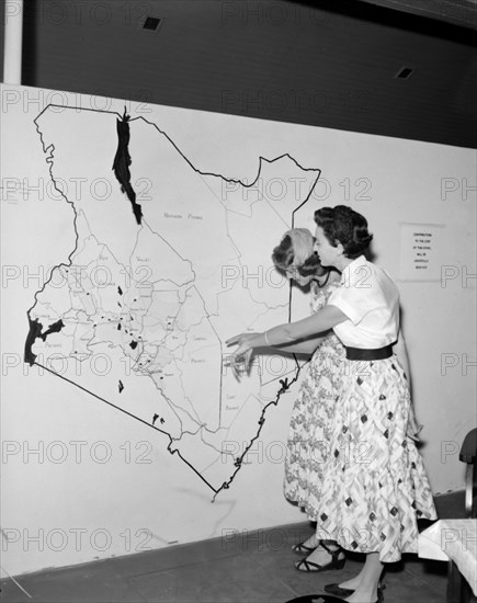Map of Kenya at the KNFU stand. Two European women point at a large scale map of Kenya displayed at the KNFU (Kenya National Farmers Union) stand at the Royal Show. Kenya, 17-20 October 1956. Kenya, Eastern Africa, Africa.