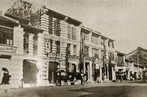 Chinese quarter in Penang. Street scene in the Chinese quarter of town. Rickshaw pullers work the street in front of a row of shops displaying signs written in Chinese script. Penang, British Malaya (Malaysia), 4-8 February 1924., Penang, Malaysia, South East Asia, Asia.