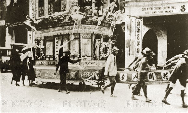 Chinese funeral carriage. An elaborately decorated funeral carriage adorned with wreaths, banners and Chinese script is pulled along a Ceylonian high street by a small procession of people at a Chinese funeral. Trincomali, Ceylon (Sri Lanka), 27-31 January 1924. Trincomali, East (Sri Lanka), Sri Lanka, Southern Asia, Asia.