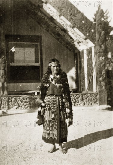 Portrait of a Maori guide. Portrait of a Maori guide outside an elaborately carved building. Identified as 'Miriam', she wears a traditional 'piupiu' (woven flax skirt) and a patterned 'tipare' (headband). Whakarewarewa, New Zealand, 10-17 May 1924. Whakarewarewa, Bay of Plenty, New Zealand, New Zealand, Oceania.