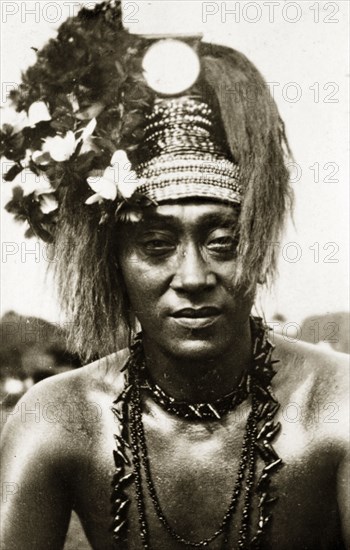 Samoan chief in 'meke' dress. Portrait of a Samoan chief wearing traditional 'meke' dress. His long hair is worn up, decorated with a beaded headdress and flowers, and his neck is adorned with long strings of beads. Suva, Fiji, 21-27 May 1924. Suva, Viti Levu, Fiji, Pacific Ocean, Oceania.