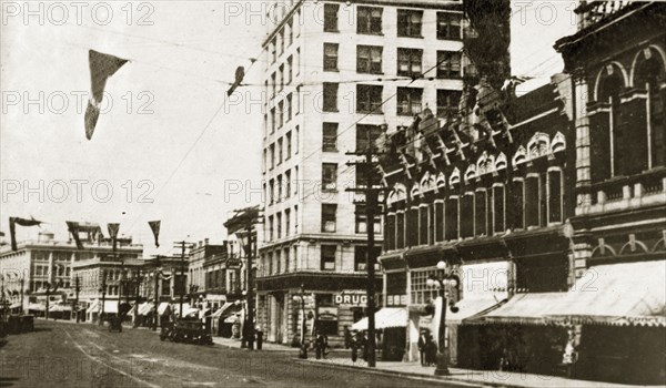 Douglas Street, Victoria. Flags hang above a quiet road lined with shopfronts identified as 'Douglas Street'. Victoria, Canada, 21 June-4 July 1924. Victoria, British Columbia, Canada, North America, North America .