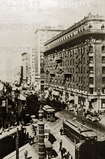 San Francisco street scene. American flags fly above a busy city street crammed with tall buildings, cars and trams. San Francisco, United States of America, 7-11 July 1924. San Francisco, California, United States of America, North America, North America .