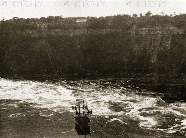 Aerial tram over Niagara Falls. An aerial tram travels on wires over the river beneath the Niagara Falls. Niagara, United States of America, 31 July-4 August 1924. Niagara Falls, New York, United States of America, North America, North America .