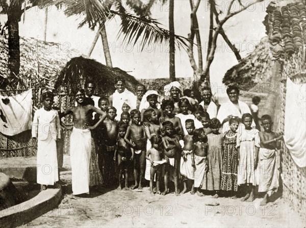 Inhabitants of a Ceylonian village. A large group of Ceylonian adults and semi-naked children gather for the camera against a backdrop of thatched village huts. Trincomoli, Ceylon (Sri Lanka), 27-31 January 1924. Trincomali, East (Sri Lanka), Sri Lanka, Southern Asia, Asia.
